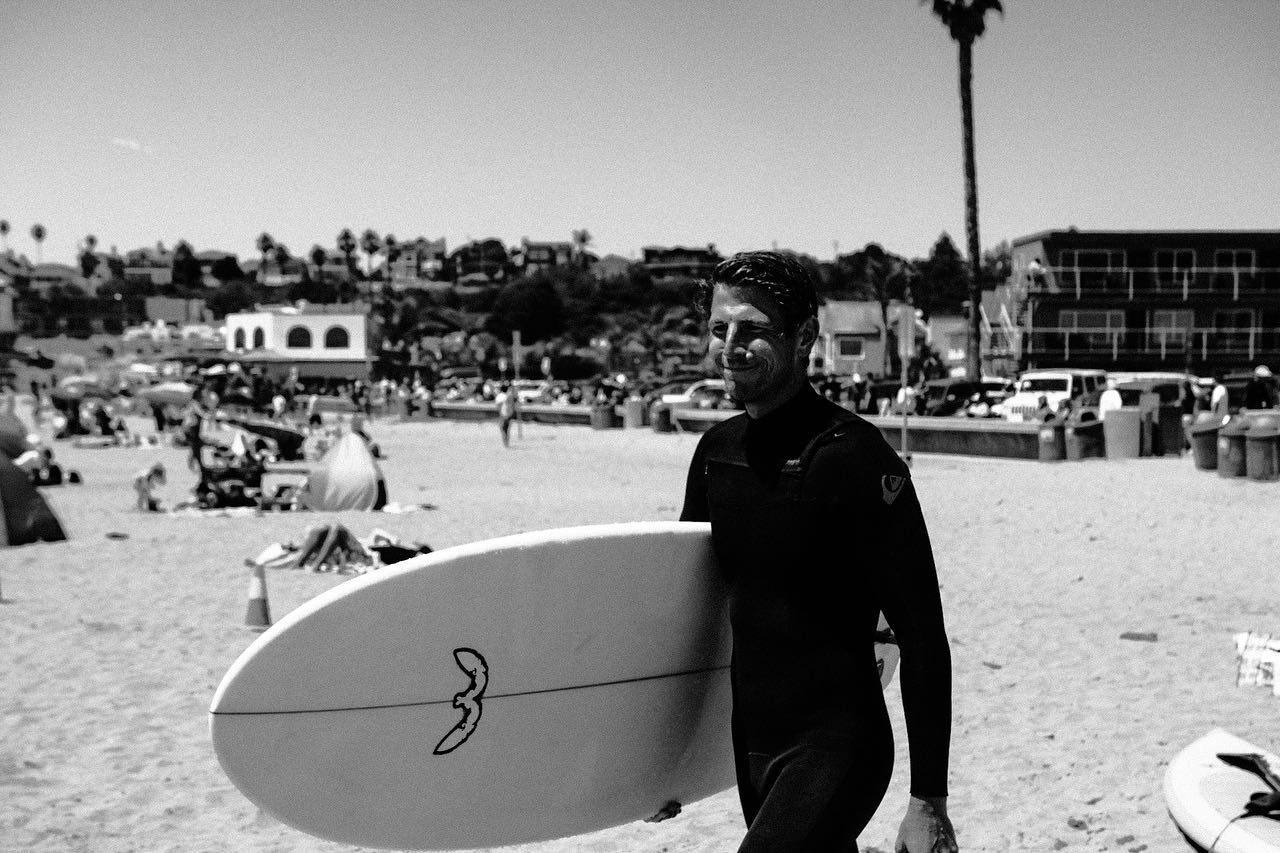A surfer carries a board up the beach past the crowd