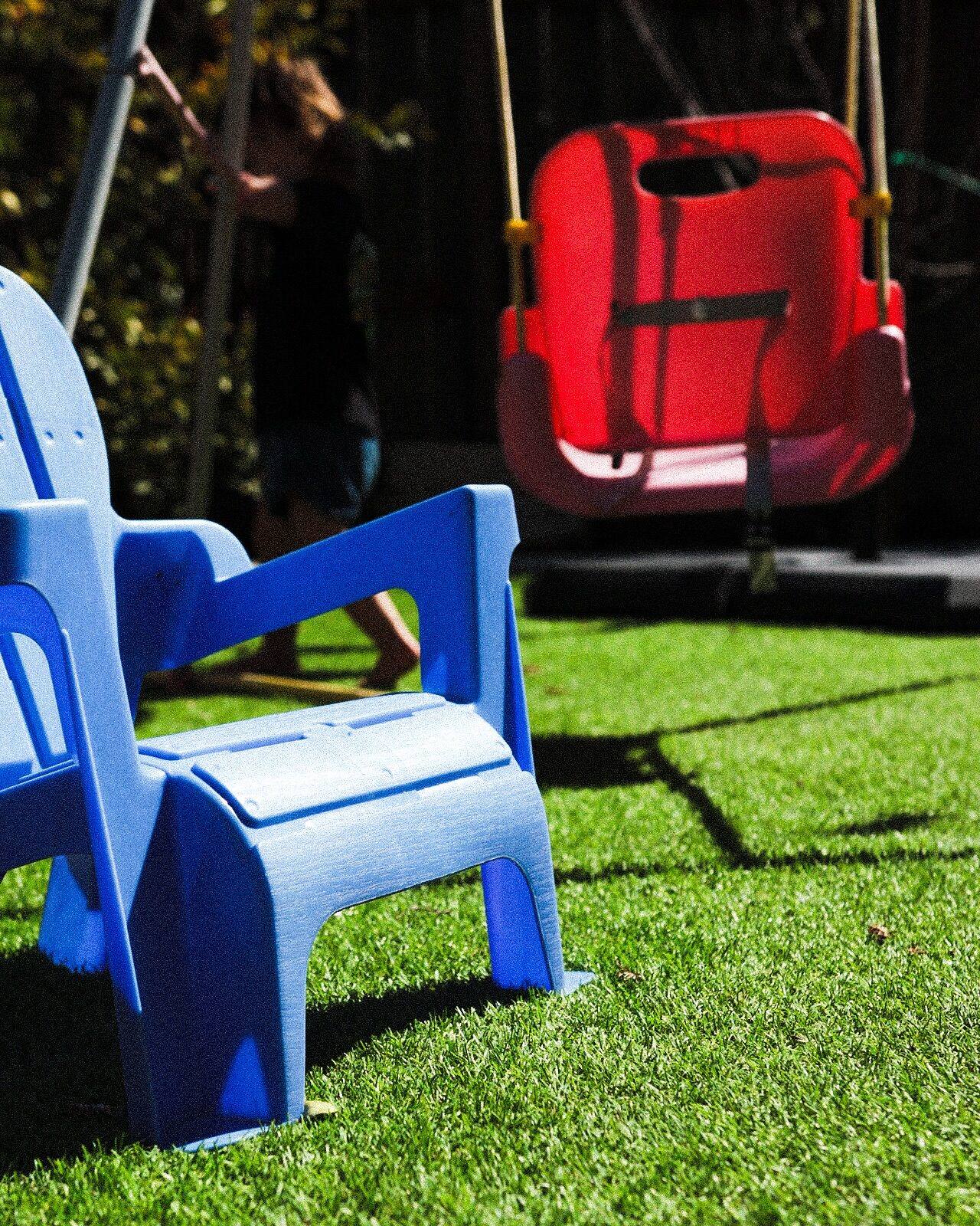 A blue plastic chair and a red swing on a lawn